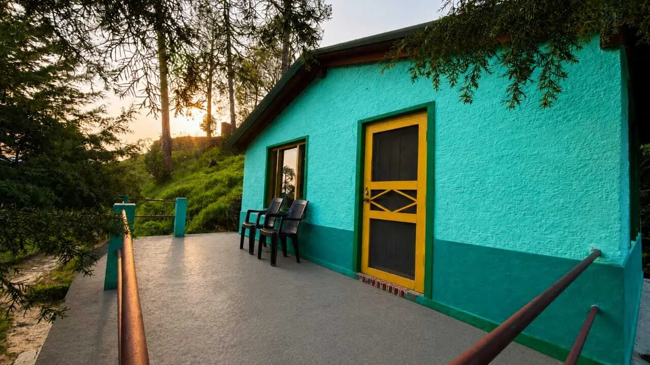 The sunlit deck of a Joshi Cottage lodge, looking out over the Binsar forest at golden hour